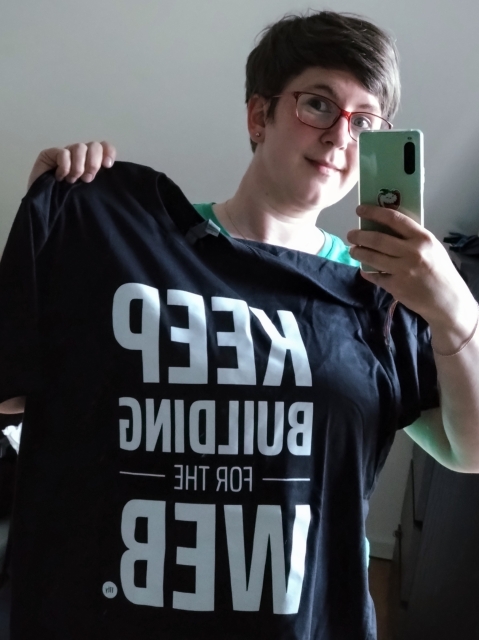 Selfie in a mirror, holding up a T shirt with the slogan "KEEP BUILDING FOR THE WEB"