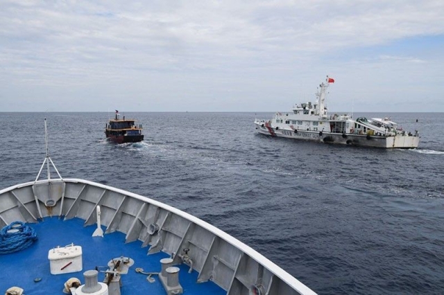 This photo taken on Aug. 22, 2023 from the deck of Philippine coast guard ship BRP Cabra shows a Chinese coast guard ship (R) shadowing a civilian boat (C) chartered by the Philippine navy to deliver supplies to Philippine navy ship BRP Sierra Madre in Second Thomas Shoal, known in the disputed South China Sea. A team of AFP journalists on board the BRP Cabra, one of the two Philippine Coast Guard escort boats, watched as one of the Chinese ships came within several meters of the vessel. AFP was one of three media outlets given the rare opportunity to join the Philippine resupply mission to Second Thomas Shoal, less than three weeks after Chinese coast guard ships water cannoned a similar replenishment operation.