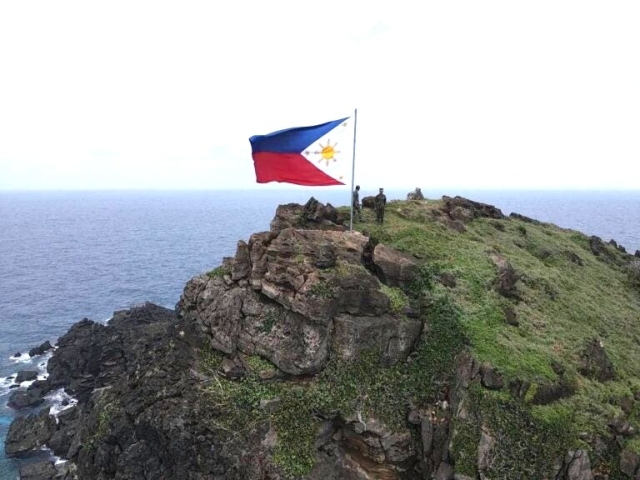 The image features a rocky cliff overlooking the ocean, with the Philippine flag flying high on top of the rocky hill. The flag is positioned towards the left side of the scene. There are two people standing on the cliff, enjoying the view and the presence of the flag.

Mavulis Island is the northernmost of the Batanes Islands and the northernmost island in the Philippines. It is part of the province of Batanes. The island is uninhabited but it is guarded by the military. It is also frequently visited by local fishermen (mostly from Itbayat and Basco) for fishing adventures.

https://en.m.wikipedia.org/wiki/Mavulis_Island