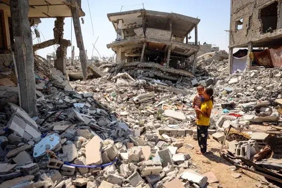 A woman holding a child amidst ruins & rubble.

[Eyad Baba/AFP]