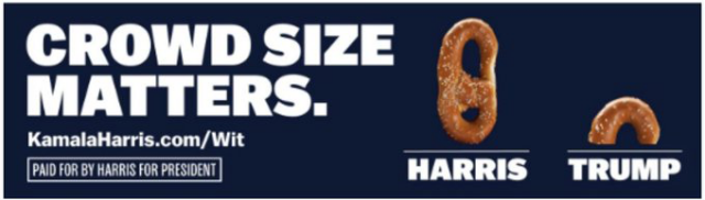 In big white block letters on black background of billboard:

"CROWD SIZE MATTERS."
KamalaHarris.com/Wit

To the right are photos of 2 pretzels: One whole one, large, with "Harris" written under it. One tiny one, with "Trump" under it.