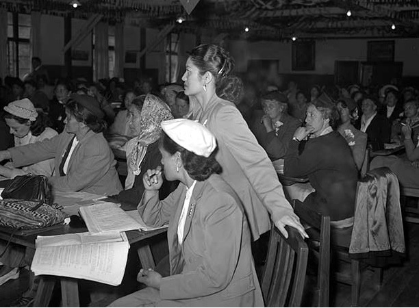 Māori women in a conference theatre that has been set up with tables.