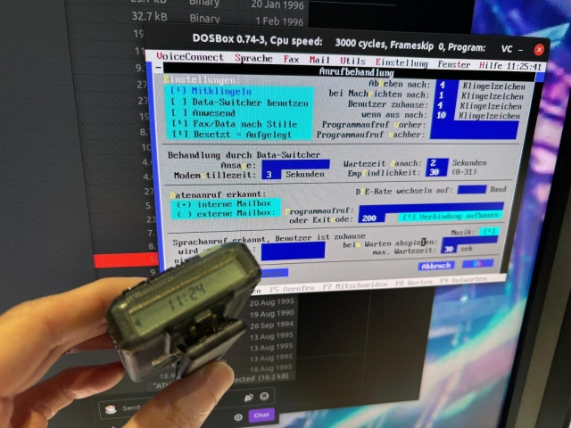 monitor with DOSBox running voiceconnect. hand holding the pager, LCD shows current time