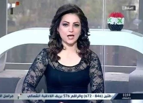 A young dark haired lady in a black dress addressing the camera in a studio in Damascus.