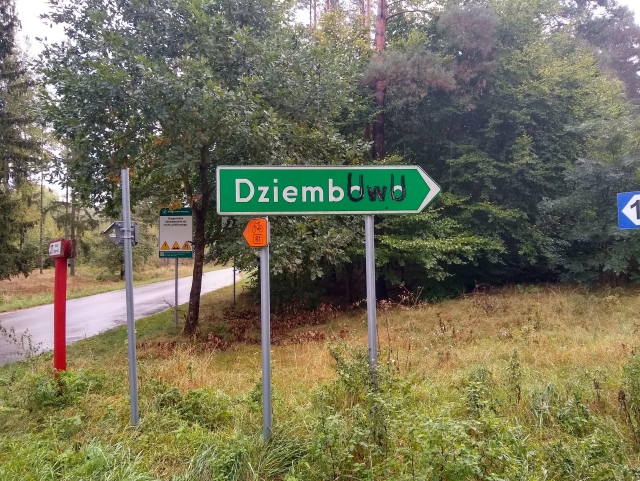 A green road sign pointing the way towards the town of Dziembowo. The ultimate letters were overwritten in black with "UwU".