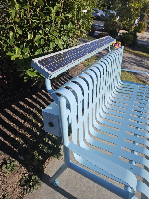 Green metal bench with solar panel along the back and usb port on the side