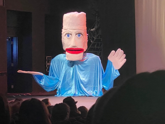 A giant puppet made to look like former Texas Governor Ann Richards, with a huge white hairdo above her face, which has comically large muppet-y eyes and bright red lips. 