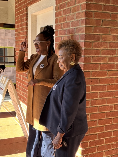 Lateefah Simon and Barbara Lee standing together on the steps of the student union building at Mills College, Oakland. Simon is talking and gesturing with great animation while Lee looks on smiling.