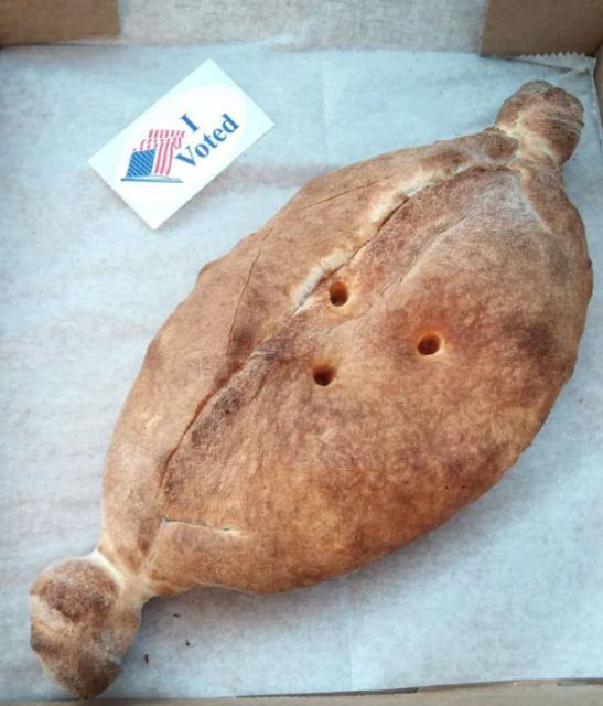 It's a pizza........thingy.

Dough ball looking thing with three holes poked into it and twists at the end. oval-shaped "I voted" sticker oriented to match.