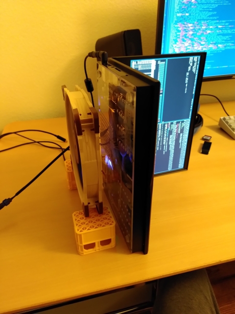 A laptop standing on it's side. A large brown fan is pointing at the laptop's under side.