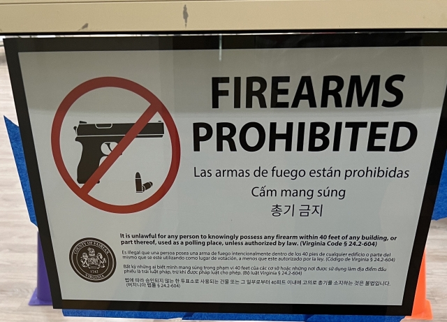 Photo of a sign in the polling place. It says. 

FIREARMS PROHIBITED
Las armas de fuego están prohibidas
Cấm mang súng
총기 금지
VIRGINIA
It is unlawful for any person to knowingly possess any firearm within 40 feet of any building, or part thereof, used as a polling place, unless authorized by law. (Virginia Code § 24.2-604)