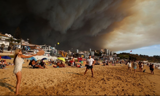 Photo from the Guardian with this caption: Holidaymakers relax on a beach at Viña del Mar on Chile’s Pacific coast under a sky darkened by forest fires.
Shows people playing a paddle game in the foreground with ominous black clouds of smoke overhead. 