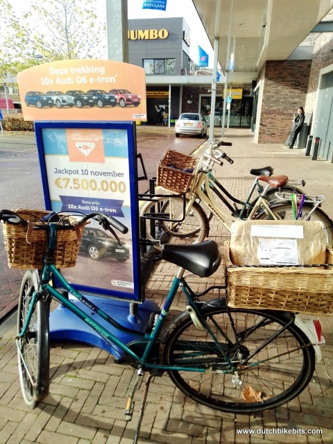 Bike parked outside the post office with a parcel visible in my rear basket. There's also an ad for lottery tickets with cars as prizes. I won't be buying any of those.