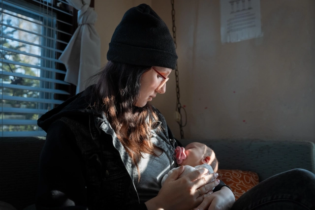 Teagan Medlin, wearing a black beanie and jacket, tenderly holds her newborn baby Audrina.