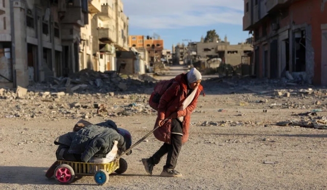 A person in a red jacket pulls a cart filled with clothing through a desolate, rubble-strewn street lined with damaged buildings.

"Northern Gaza Strip, this week. How does a person find the strength to rise within the horror? 

Photo: Omar AL-QATTAA / AFP"
