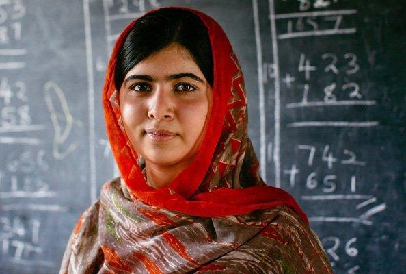 press photo of Malala in front of a chalkboard with maths on it. She is a Pakistani woman wearing a shayla - a loosely wrapped headscarf.