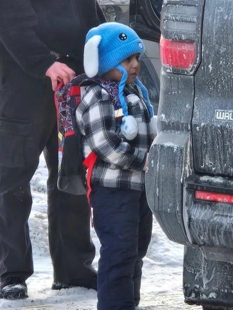 A picture of 5-year-old Liam Ramos, in a blue bunny hat and backpack standing outside an SUV, with an ICE agent standing behind him. Photo of Columbia Heights Public Schools