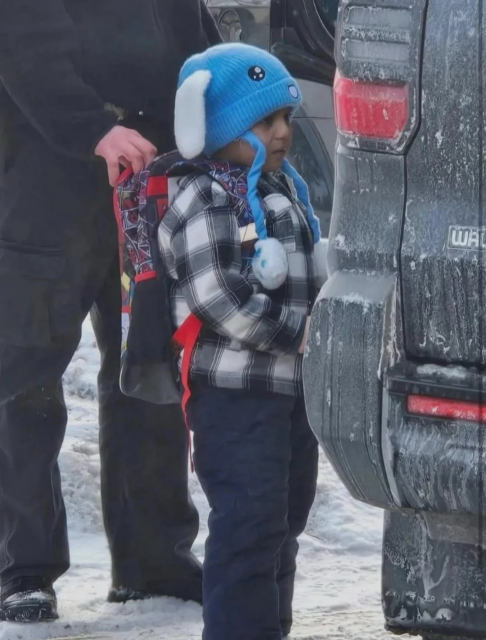 Photo of Liam Ramos in a blue hat and plaid jacket being put in a dark vehicle 