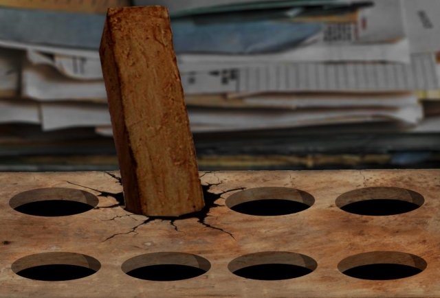 A pegboard into which a square peg has been jammed, cracking the surface. The background is a messy, indistinct pile of papers.