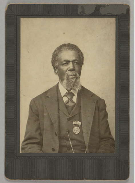 A cabinet card of a 19th century Black man, Thomas Peterson. Peterson is looking at the camera and wearing a three-piece suit with a medal attached to the left side of the vest. The medal was presented to Peterson in 1884 by the residents of Perth Amboy, N.J. in recognition of his status as the first African American voter in the United States under the provisions of the Fifteenth Amendment. The albumen print is attached to a stiff card backer with wear showing around the edges. There is a printed label on the verso that reads, "Inscription on the Medal. Presented by citizens of Perch Amboy, N.J., to Thomas Peterson, the first colored voter in the United States under the provisions of the Fifteenth Amendment, at an election held in that city March 31st, 1870." The cabinet card was printed as a memento for the medal presentation ceremony. 