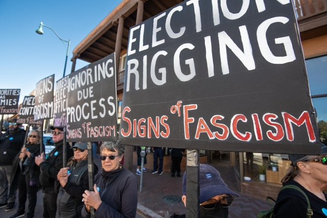 People dressed in black stretched along the street holding black and white signs with statements like “Election Rigging - Sign of Fascism”.