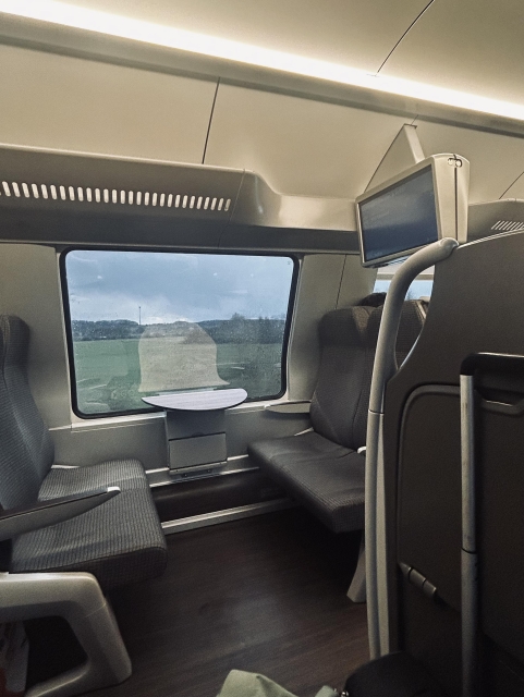 A picture of empty train seats with a small rounded table. A green landscape in the window in the background. 