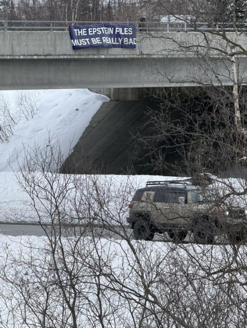 A sign over a highway in Eagle River, Alaska, reading, "The Epstein files must be really bad," commenting on how Trump has gone to war against Iran to distract us from what is revealed by the Epstein files