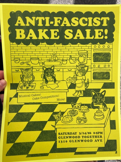 Hand holding a yellow flyer that says in bold letters “Anti-Fascist Bake Sale.” On the flyer is a scene of a kitchen with a bunch of cats baking. The flyer announces that there will be “musical cakes, cake competitions, and more.”