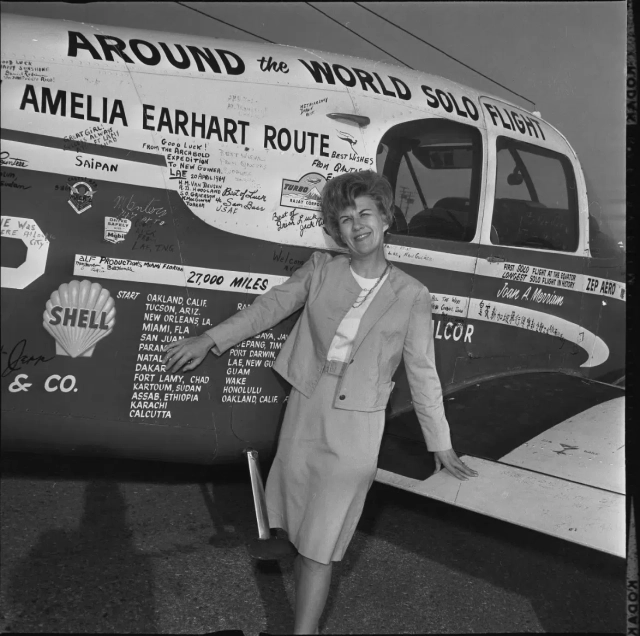 Joan Merriam Smith with her plane the “City of Long Beach.” She is a white woman with blonde bouffant hair. The plane is covered with writing including her planned route and messages of good luck.

Photo credit: UCLA Library Special Collections, Charles E. Young Research Library.