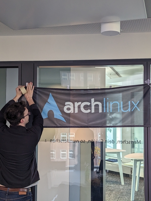 A person pretending to out up a banner. The banner has "Arch Linux" on it.
